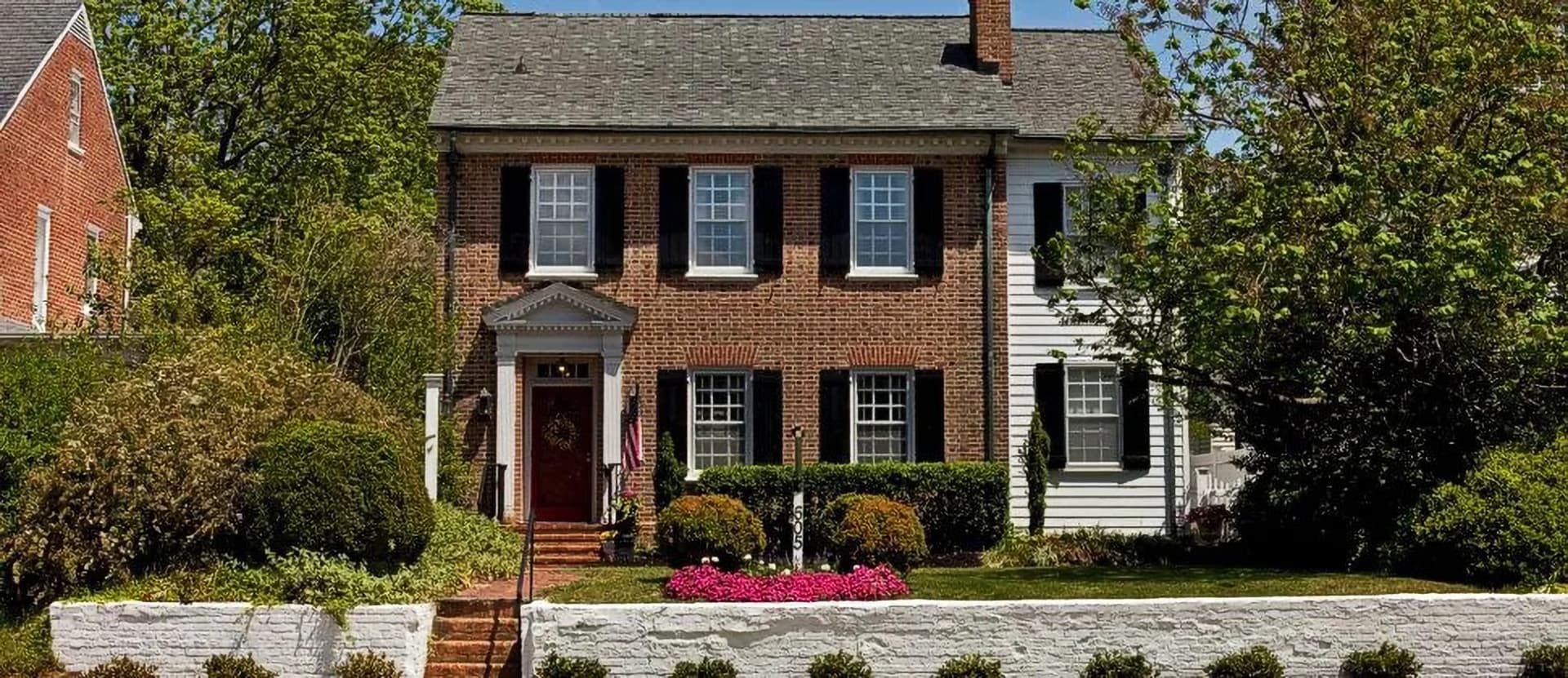 A two-story brick house with white trim and a front garden featuring flowers.